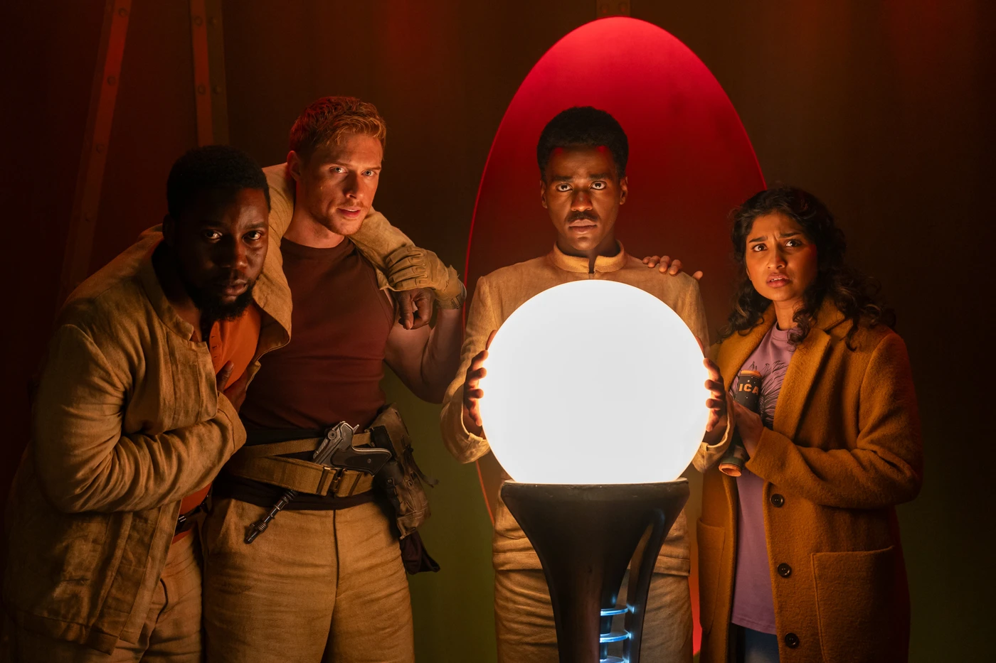 Ncuti Gatwa as The Doctor surrounded by other characters putting his hands on a giant glowing orb. 
